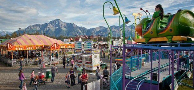 Rides and food vendors at the Alaska State Fair with mountains in the background. Westmark Hotels