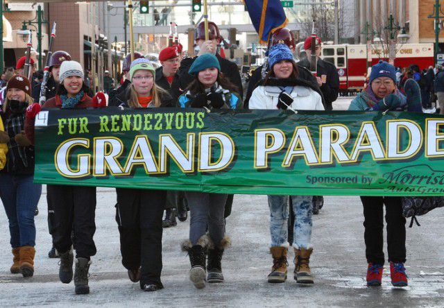 kids holiding a grand parade sign walking down snowy streets