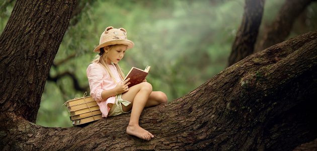 A girl reads a book while sitting in a tree.